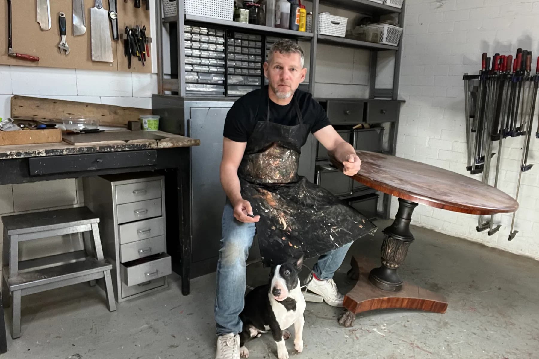 Arjen Eissens in his furniture-restoration workshop in Weesp, with his dog and a restored table top.